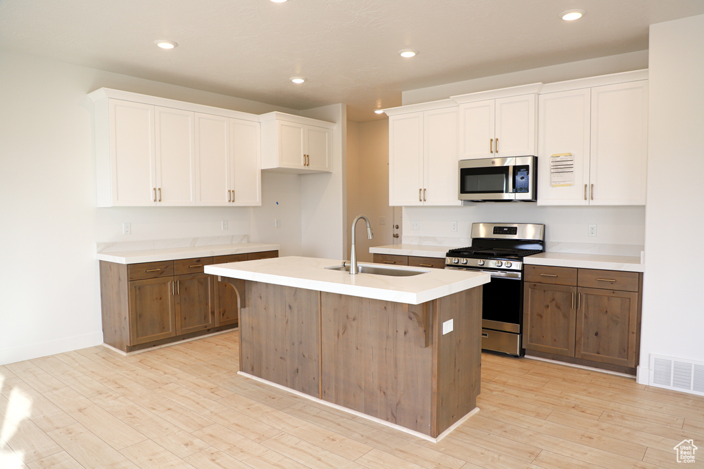 Kitchen with stainless steel appliances, white cabinetry, light wood finished floors, light countertops, and a kitchen island with sink
