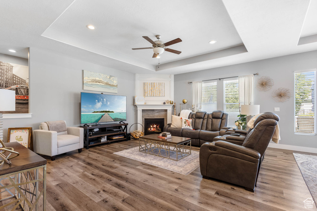 Living room featuring a tray ceiling, wood finished floors, a ceiling fan, a lit fireplace, and recessed lighting