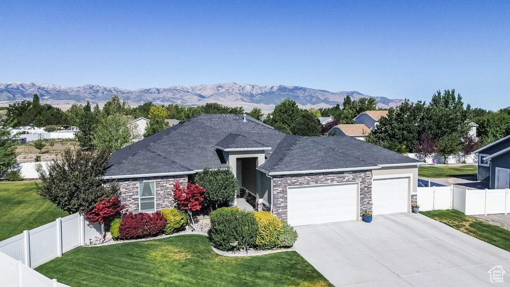 Single story home with a garage, stone siding, driveway, a mountain view, and a shingled roof