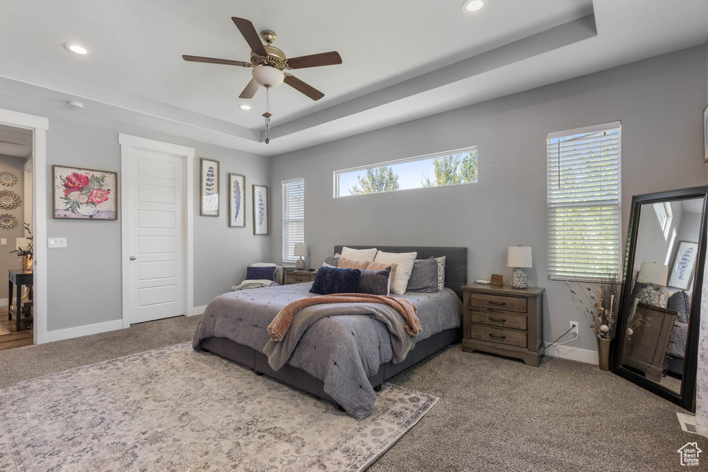 Carpeted bedroom featuring a raised ceiling, recessed lighting, multiple windows, and a ceiling fan