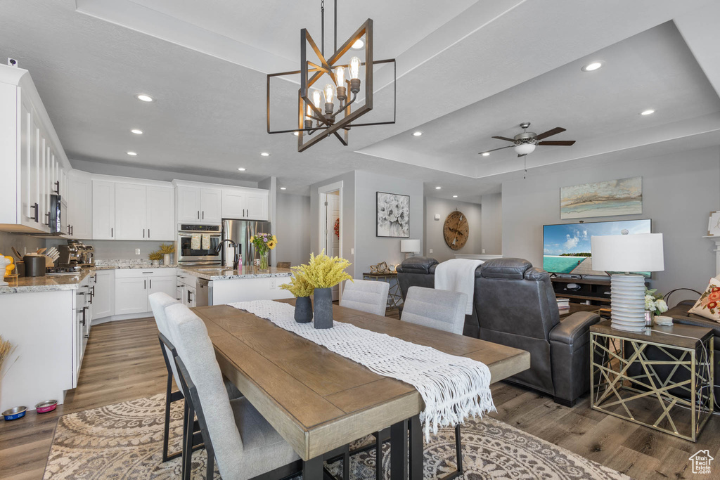 Dining room featuring wood finished floors, recessed lighting, a raised ceiling, a ceiling fan, and a chandelier