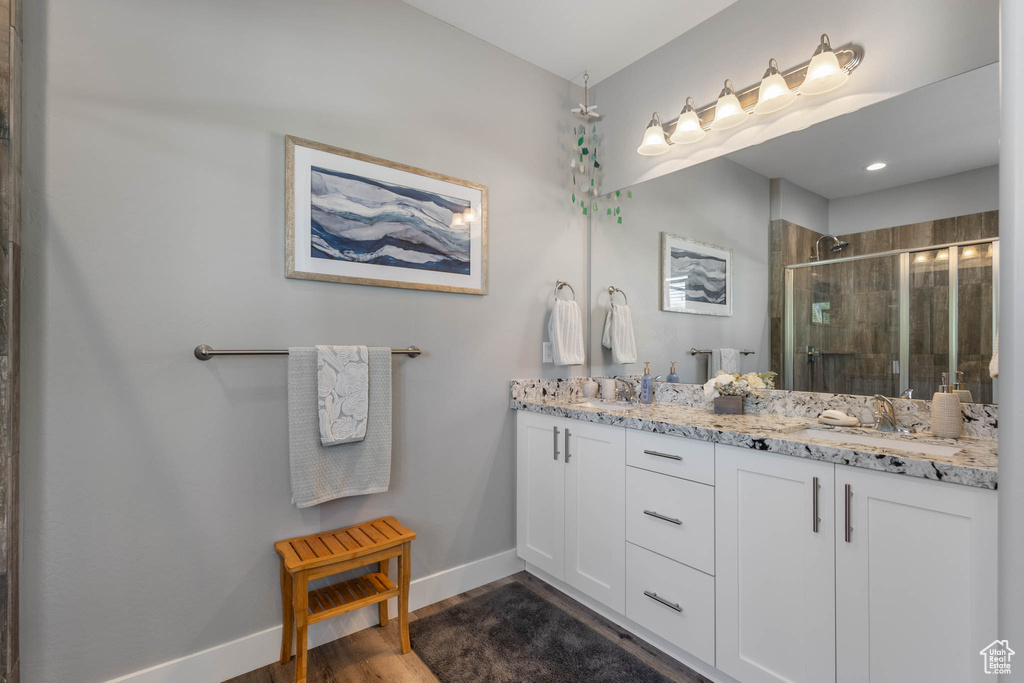 Full bathroom with double vanity, a stall shower, and wood finished floors