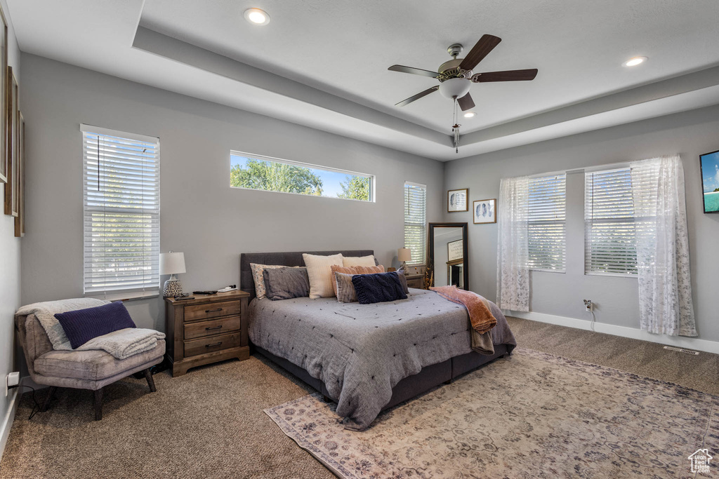 Bedroom with carpet flooring, a raised ceiling, multiple windows, recessed lighting, and a ceiling fan