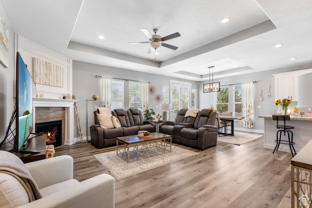 Living room featuring a tray ceiling, healthy amount of natural light, light wood-style floors, a ceiling fan, and recessed lighting