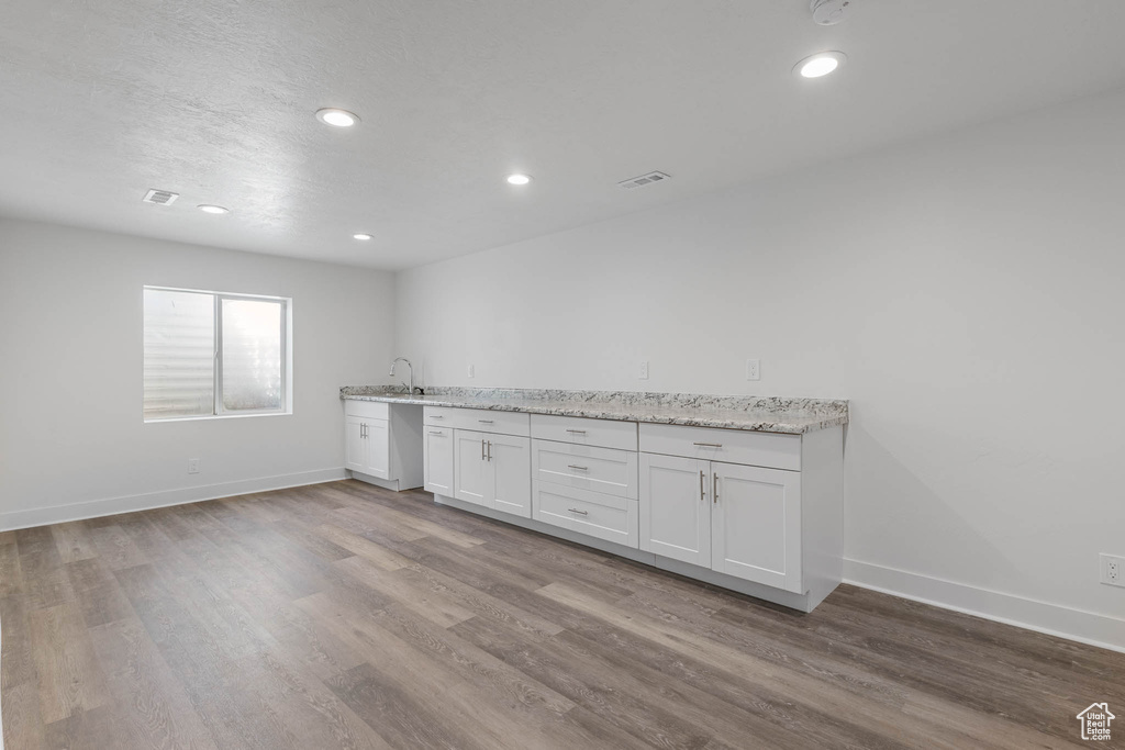 Kitchen with wood finished floors, white cabinetry, light stone countertops, recessed lighting, and stainless steel dishwasher