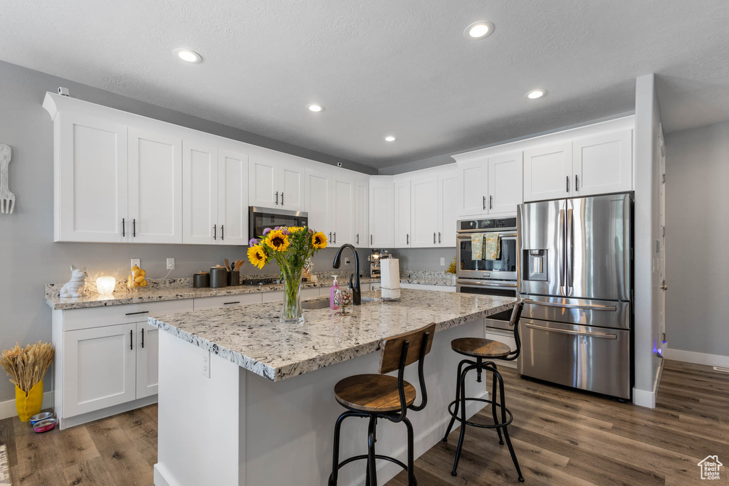 Kitchen featuring stainless steel appliances, dark wood finished floors, white cabinetry, recessed lighting, and a breakfast bar