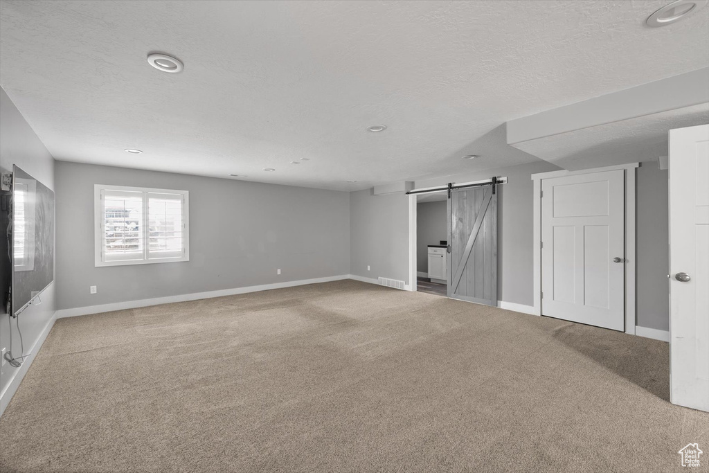Basement with a barn door, carpet floors, recessed lighting, and a textured ceiling