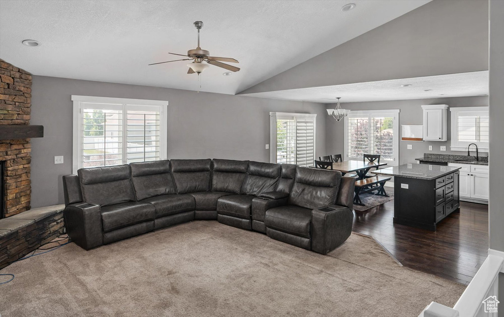 Living room with a ceiling fan, vaulted ceiling, a chandelier, a fireplace, and dark wood-type flooring