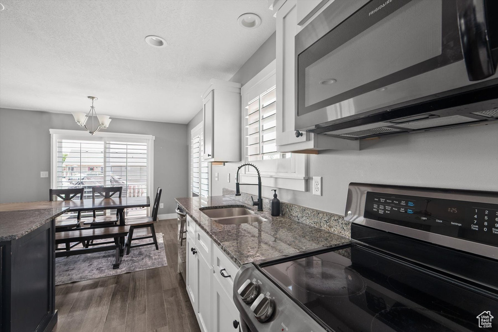 Kitchen with stainless steel appliances, dark wood finished floors, white cabinetry, dark stone counters, and decorative light fixtures