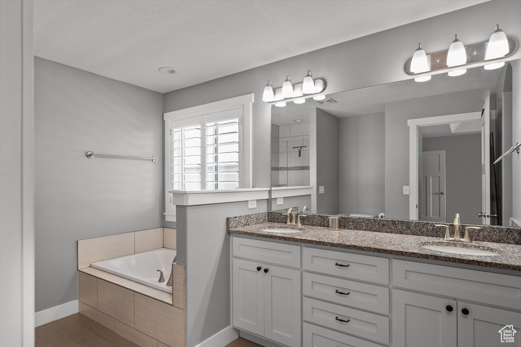 Full bathroom featuring double vanity, a bath, tiled shower, and wood finished floors