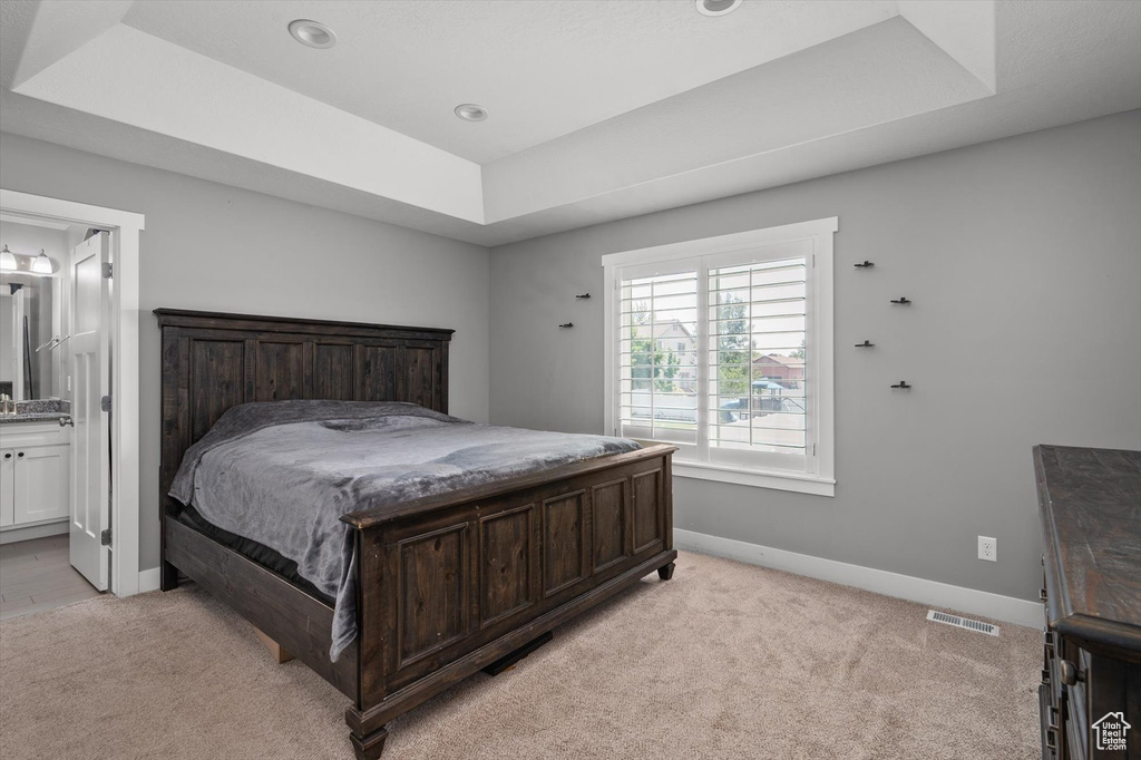 Bedroom with a raised ceiling, light colored carpet, and connected bathroom
