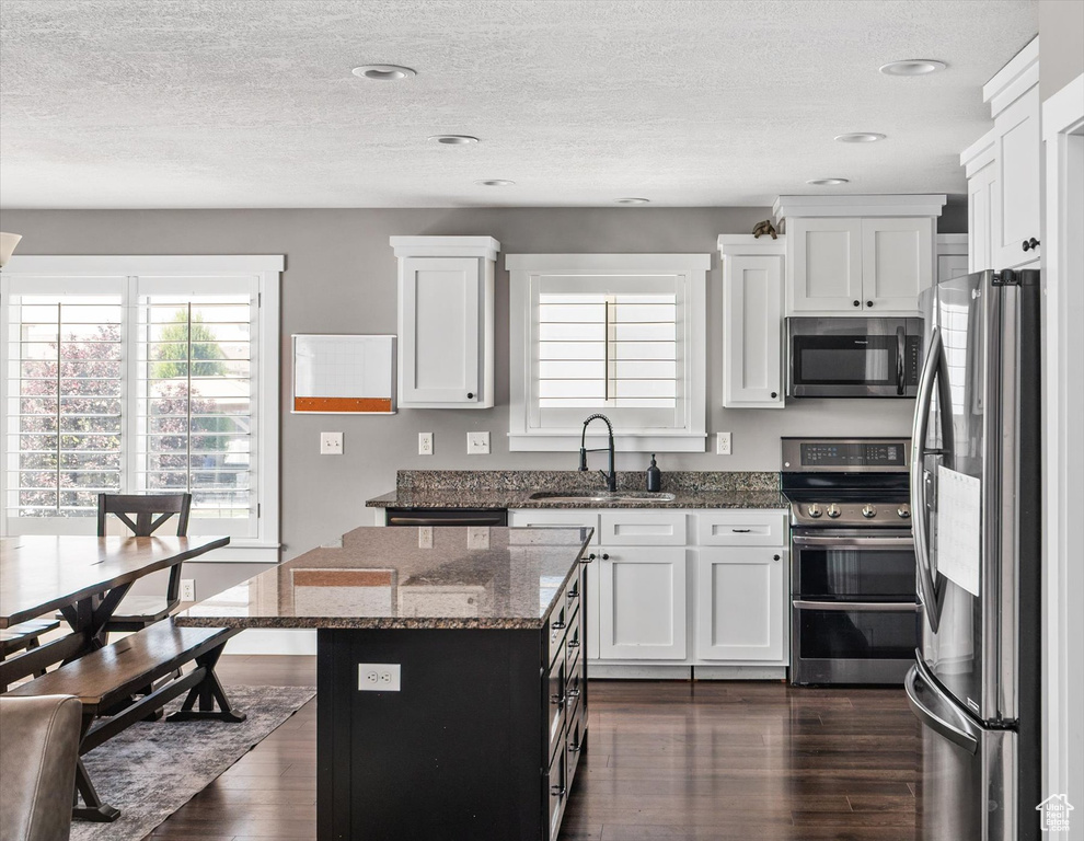 Kitchen with appliances with stainless steel finishes, dark wood finished floors, dark stone counters, white cabinets, and a center island