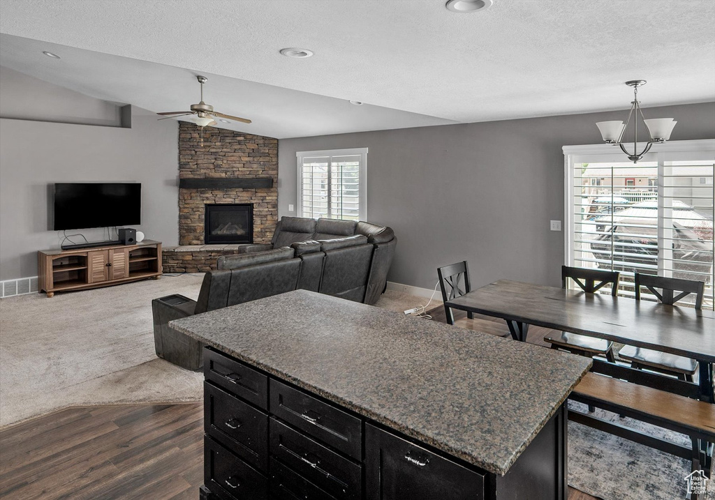 Kitchen with a ceiling fan, dark cabinets, dark wood finished floors, a stone fireplace, and a textured ceiling