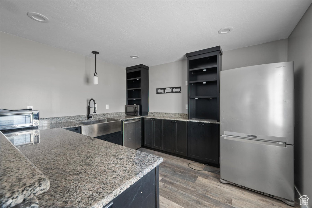 Kitchen featuring stainless steel appliances, light wood-style floors, light stone counters, recessed lighting, and dark cabinets