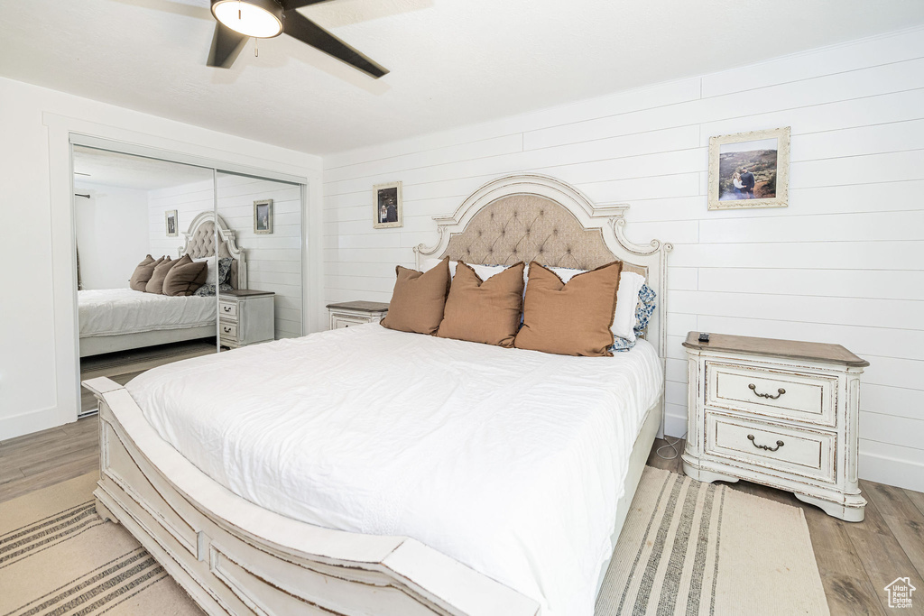 Bedroom featuring light wood-style floors, a closet, ceiling fan, and wood walls