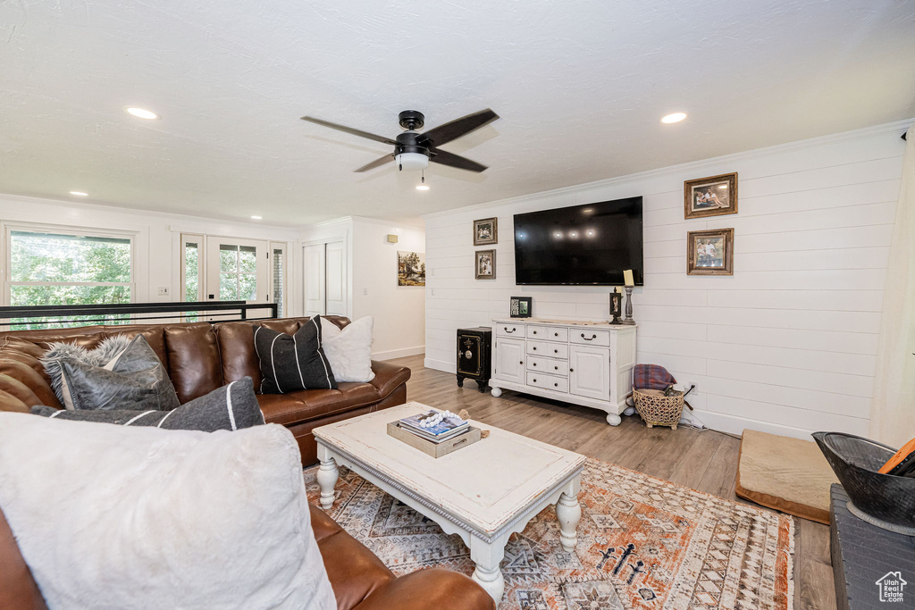 Living room featuring light wood finished floors, wooden walls, a ceiling fan, and recessed lighting