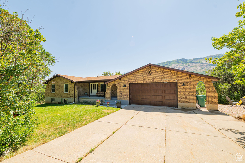 Single story home with brick siding, an attached garage, a front lawn, concrete driveway, and a mountain view
