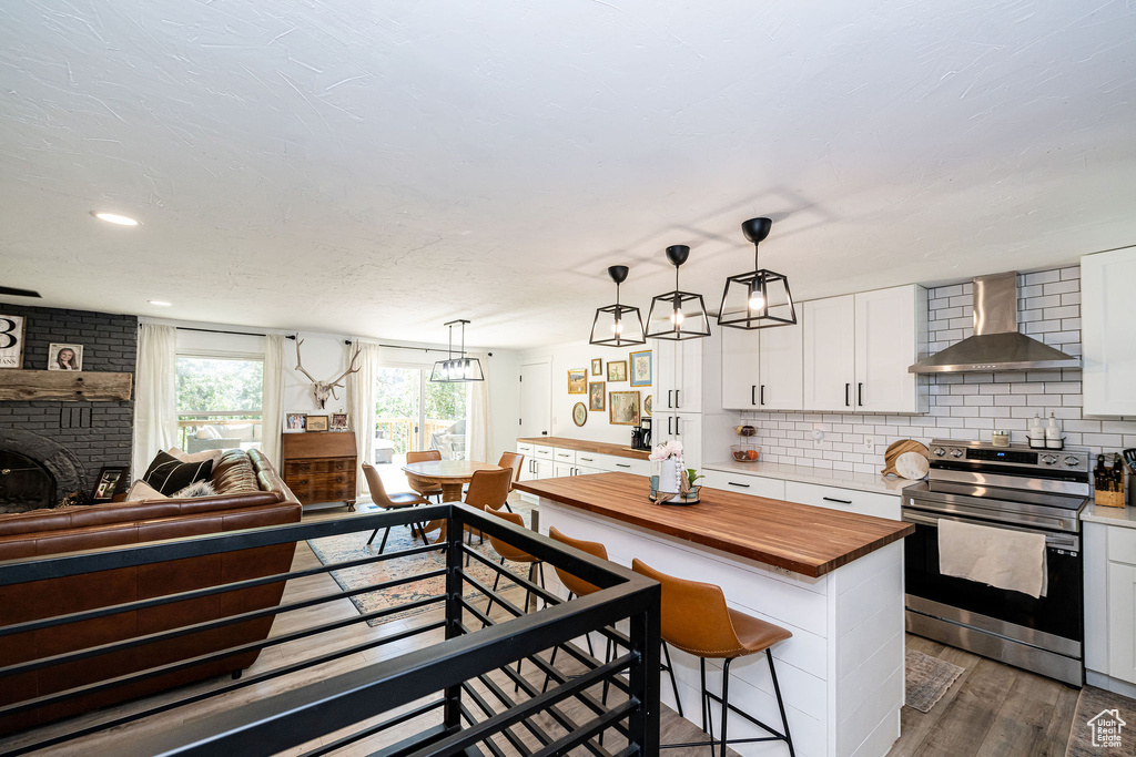 Kitchen with stainless steel range with electric cooktop, wall chimney range hood, butcher block counters, open floor plan, and white cabinets