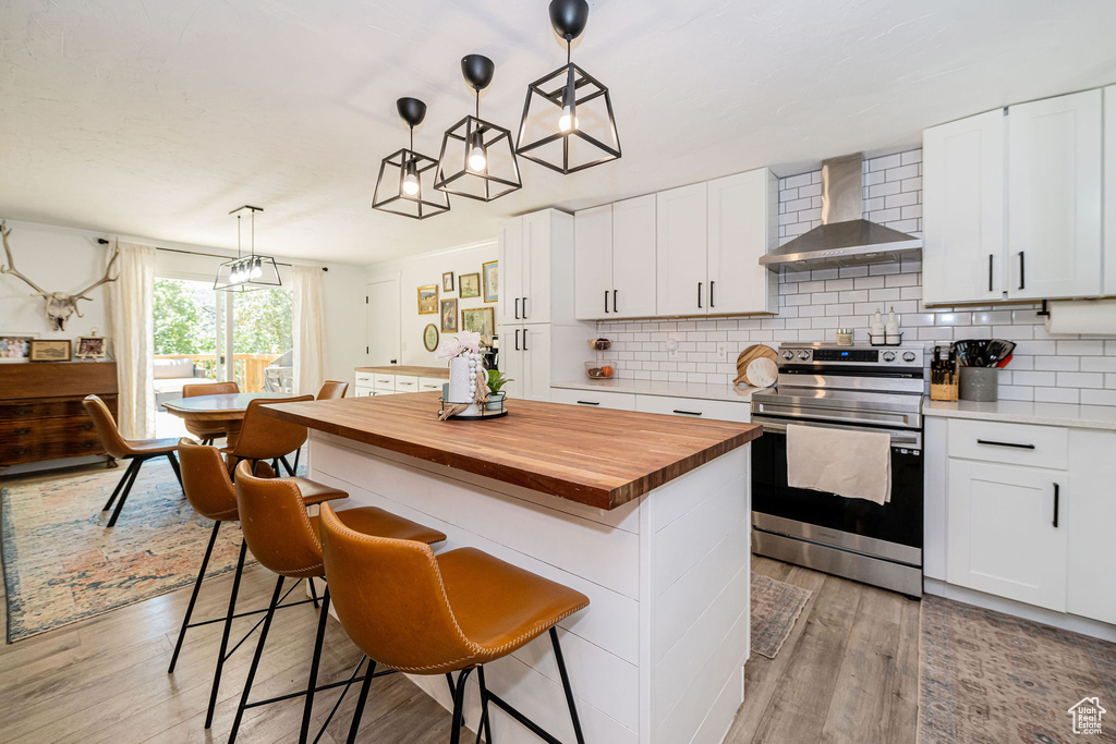 Kitchen with wall chimney exhaust hood, stainless steel range with electric cooktop, light wood finished floors, and butcher block counters
