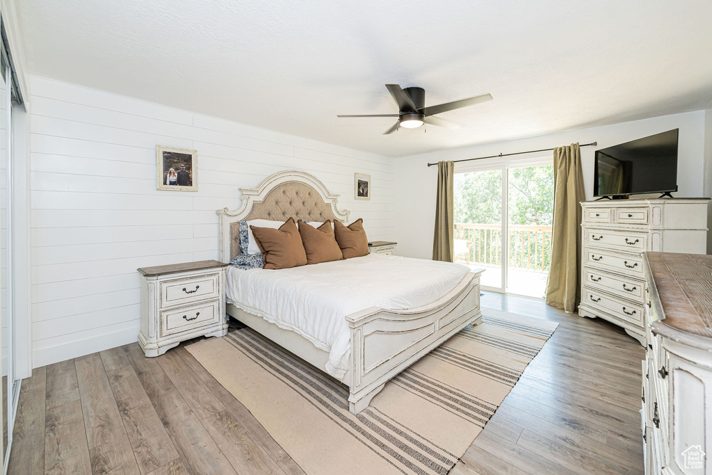 Bedroom featuring access to outside, light wood-style flooring, wooden walls, and ceiling fan