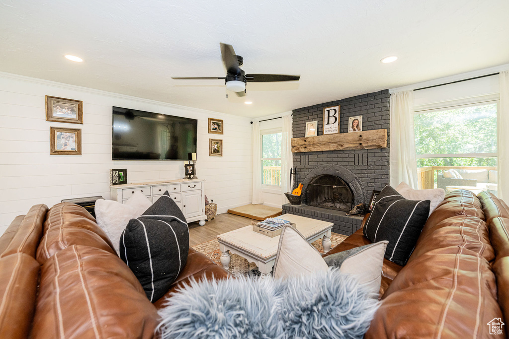 Living room with wood finished floors, healthy amount of natural light, a ceiling fan, a brick fireplace, and wooden walls