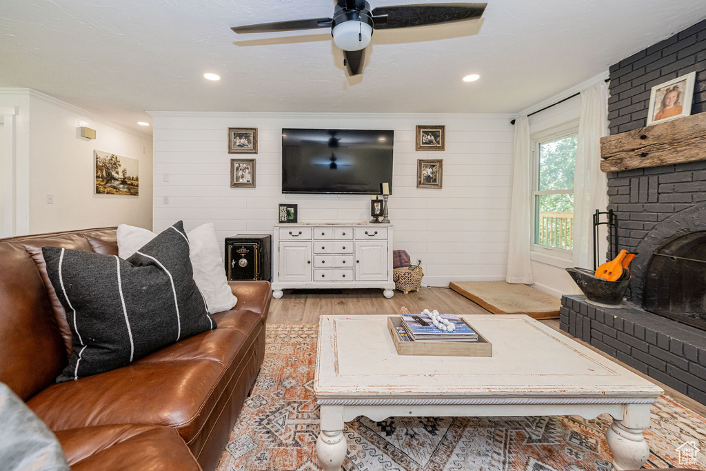 Living room featuring light wood-style floors, crown molding, a brick fireplace, a ceiling fan, and recessed lighting