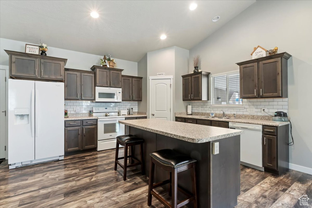 Kitchen with white appliances, dark brown cabinets, a center island, dark wood finished floors, and light countertops