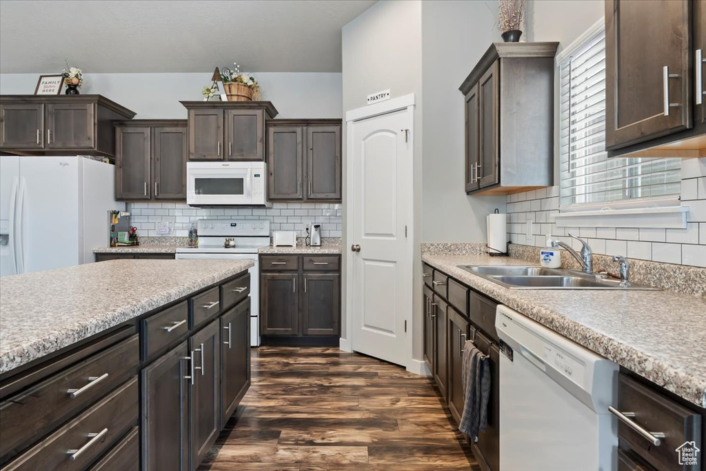 Kitchen with white appliances, dark brown cabinets, dark wood-style flooring, light countertops, and backsplash