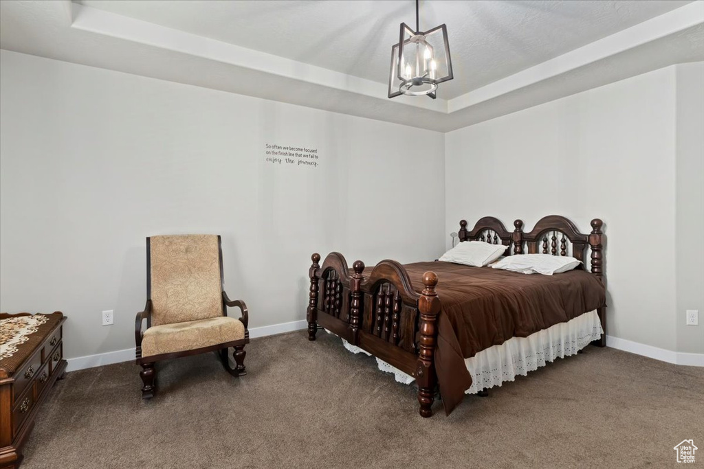 Carpeted bedroom featuring a tray ceiling and a chandelier