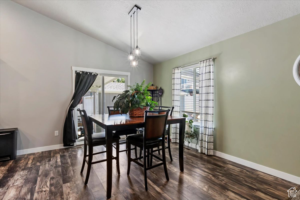 Dining space with vaulted ceiling, dark wood finished floors, and a textured ceiling