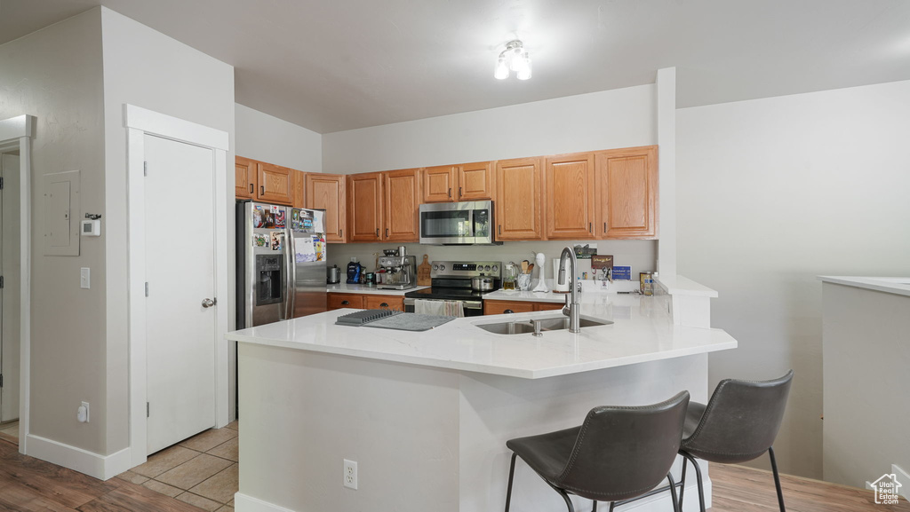 Kitchen featuring stainless steel appliances, a peninsula, a kitchen breakfast bar, electric panel, and light wood-style flooring