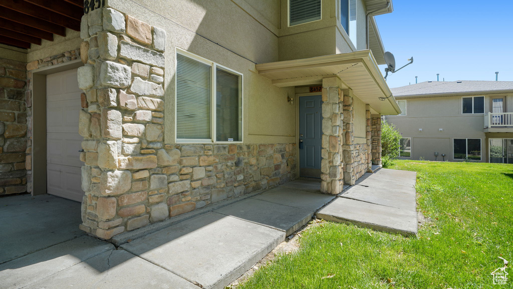 Doorway to property with stone siding, a garage, and a yard