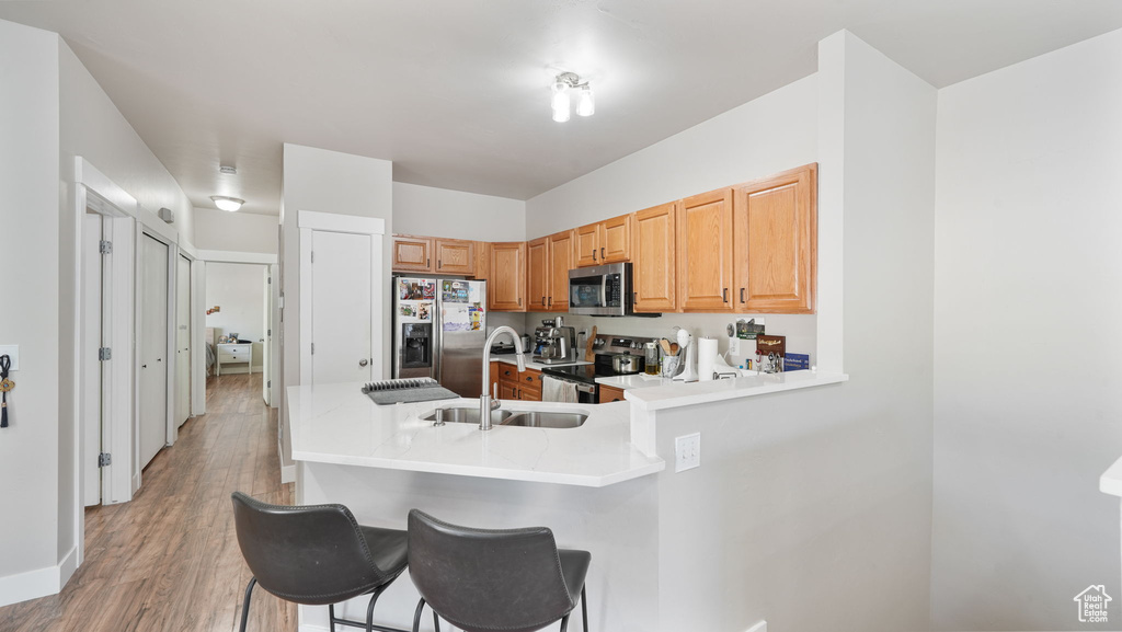 Kitchen featuring appliances with stainless steel finishes, a peninsula, a kitchen bar, and light wood-style flooring