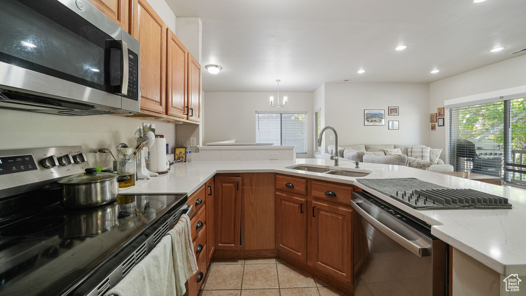 Kitchen featuring stainless steel appliances, light tile patterned flooring, a chandelier, a peninsula, and light stone countertops