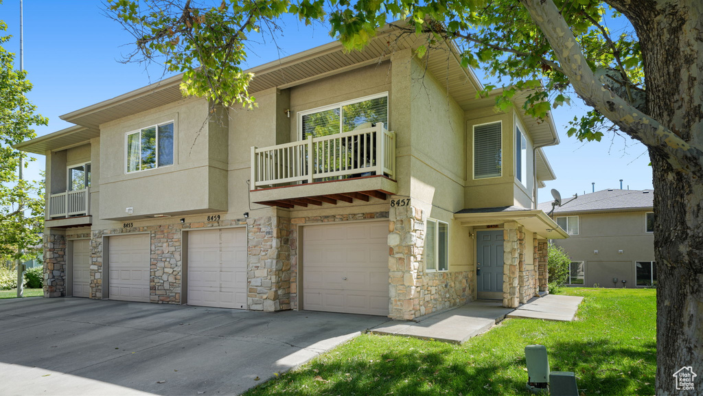 View of front of property with stone siding, a garage, a balcony, stucco siding, and driveway