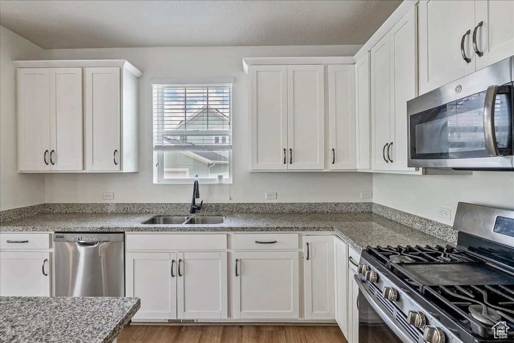 Kitchen with stainless steel appliances, white cabinetry, light wood-style flooring, and light stone countertops