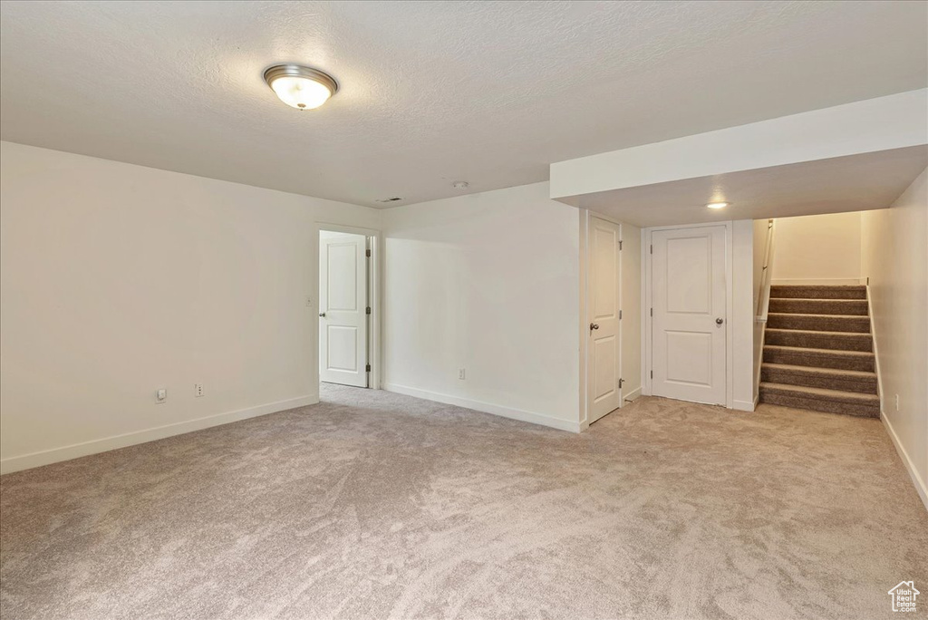 Empty room featuring light carpet, stairs, and a textured ceiling