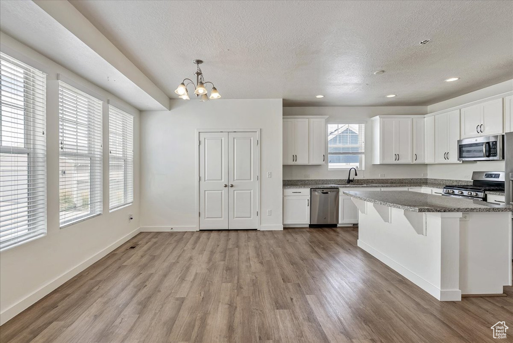 Kitchen with appliances with stainless steel finishes, a textured ceiling, light wood-style floors, a chandelier, and white cabinets