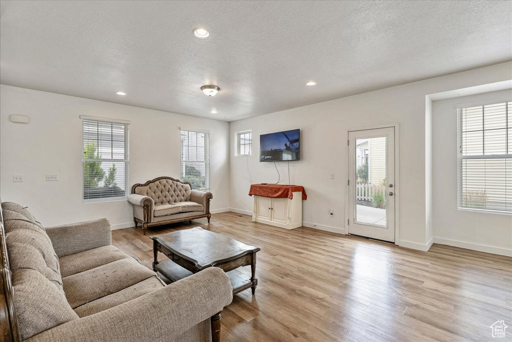 Living area with light wood-style flooring, healthy amount of natural light, a textured ceiling, and recessed lighting