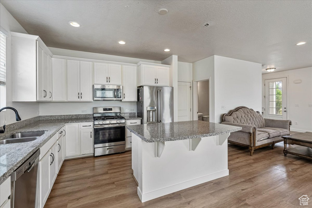 Kitchen featuring appliances with stainless steel finishes, a kitchen island, dark wood-type flooring, open floor plan, and white cabinets