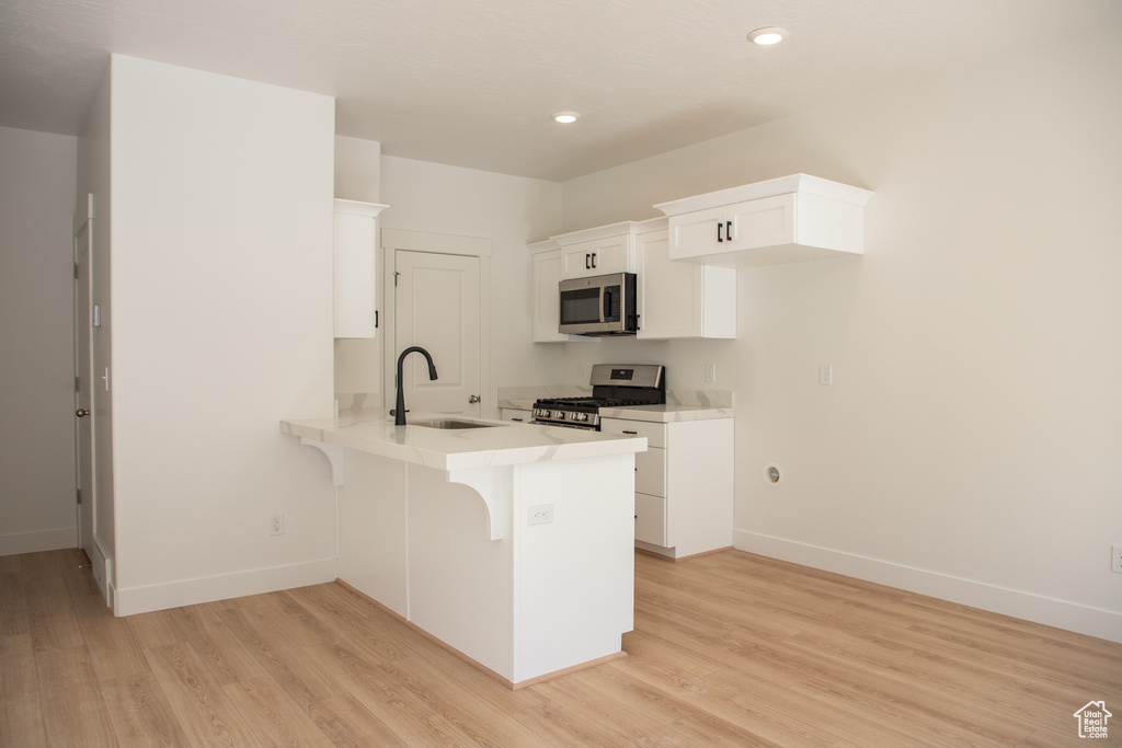 Kitchen with stainless steel appliances, a peninsula, a kitchen bar, white cabinetry, and light countertops