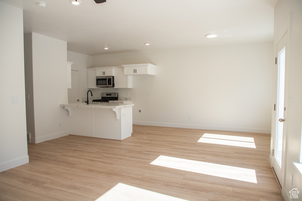 Kitchen with stainless steel appliances, a peninsula, a kitchen bar, white cabinetry, and light countertops