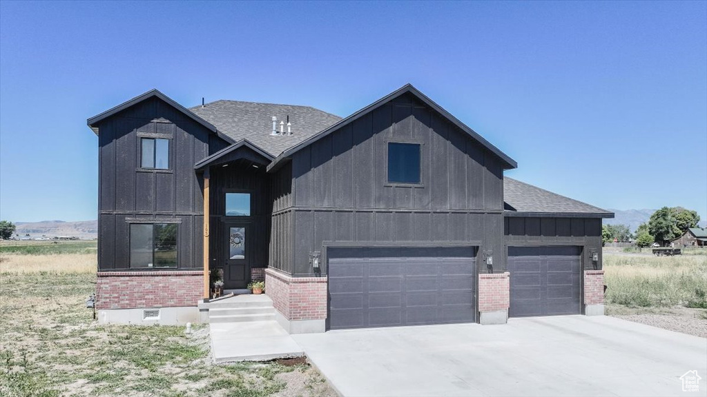 Modern inspired farmhouse with brick siding, board and batten siding, a shingled roof, concrete driveway, and a garage