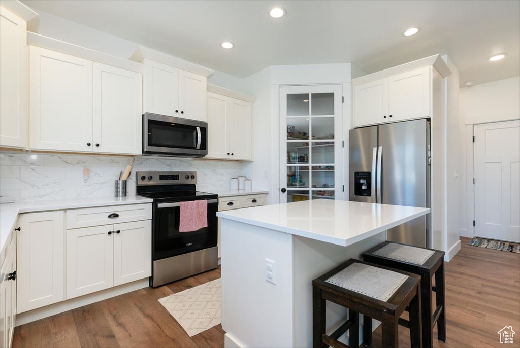 Kitchen featuring stainless steel appliances, dark wood-style flooring, a kitchen bar, tasteful backsplash, and white cabinets