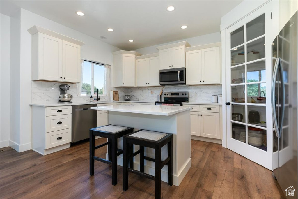 Kitchen with stainless steel appliances, backsplash, white cabinetry, dark wood finished floors, and recessed lighting