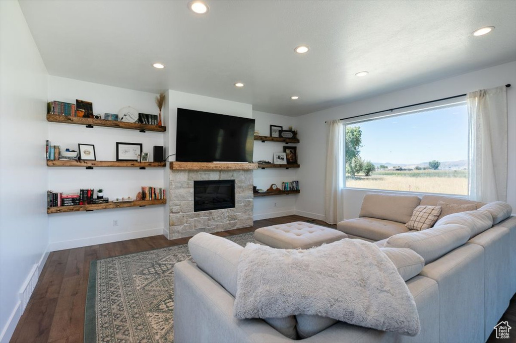 Living room with dark wood finished floors, recessed lighting, and a stone fireplace