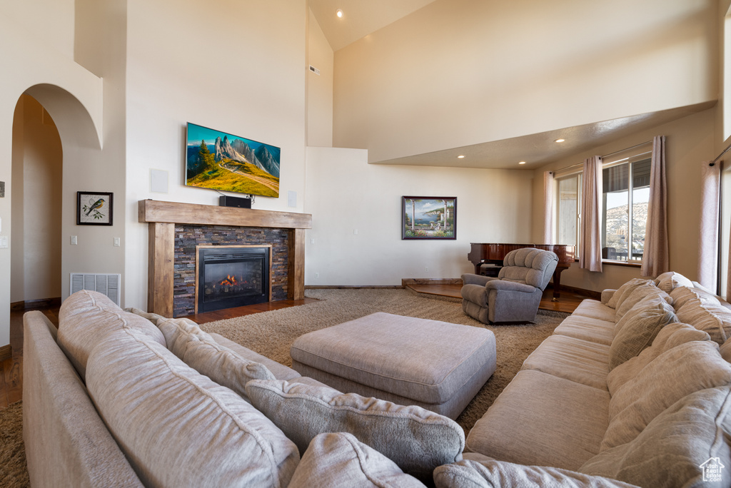 Living room featuring high vaulted ceiling, arched walkways, a fireplace, wood finished floors, and recessed lighting