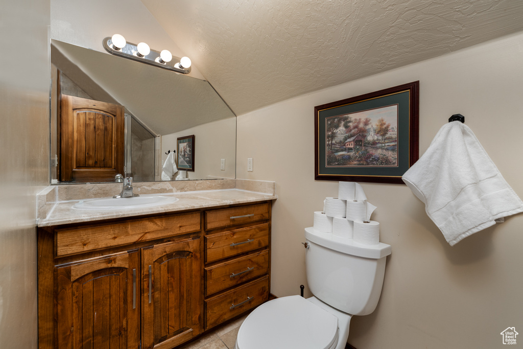Bathroom featuring lofted ceiling, vanity, tile patterned flooring, and a textured ceiling