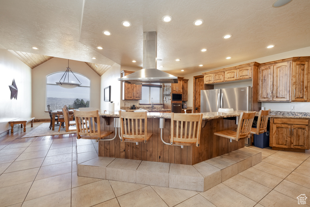 Kitchen featuring freestanding refrigerator, island range hood, recessed lighting, light tile patterned flooring, and light stone counters