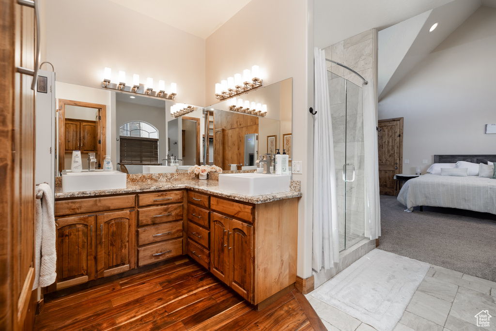Bathroom featuring a stall shower, high vaulted ceiling, double vanity, and ensuite bath